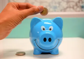 hand placing a coin into a blue piggy bank