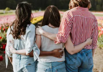 three girls looking at a field of flowers with their arms around each other