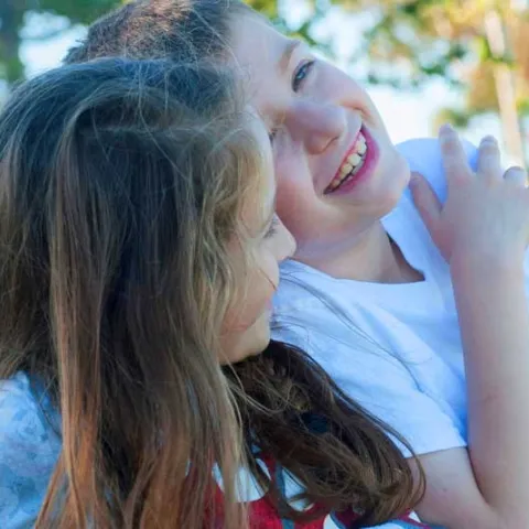 siblings hugging and laughing while playing outside with a Mickey Mouse toy