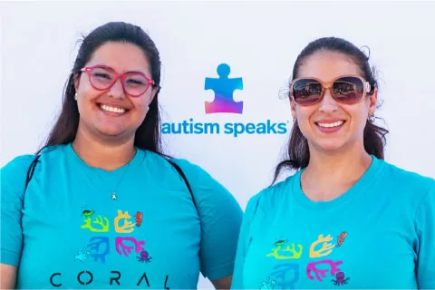 2 women in glasses in front of Autism Speaks sign