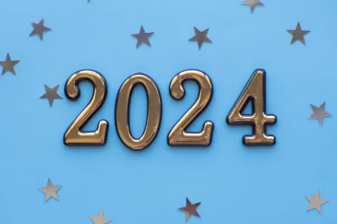 gold 2024 letters against light blue background with small metallic stars scattered in background