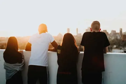 4 teens on a rooftop overlooking a city at sunset