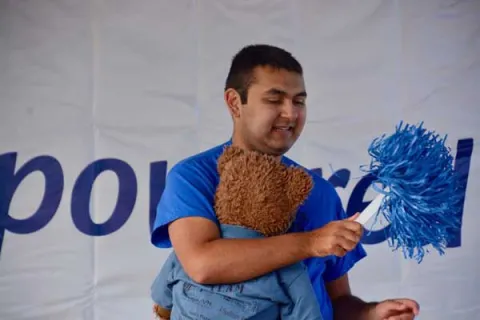 Andrew at an Autism Speaks Walk holding a stuffed bear and blue pom-pom