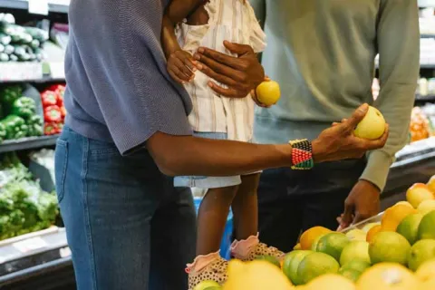 Black parents looking at produce in the supermarket with their young daughter