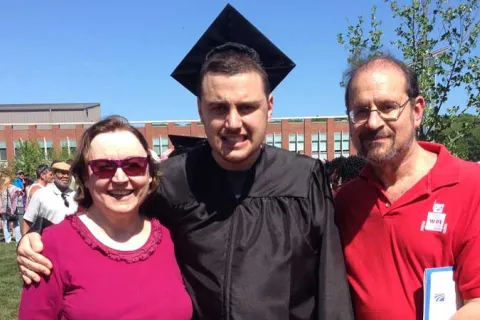 Ian H. wearing his cap and gown at graduation with his parents