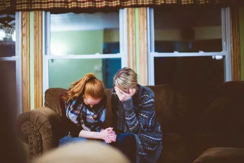 Sad people sitting on a couch comforting each other