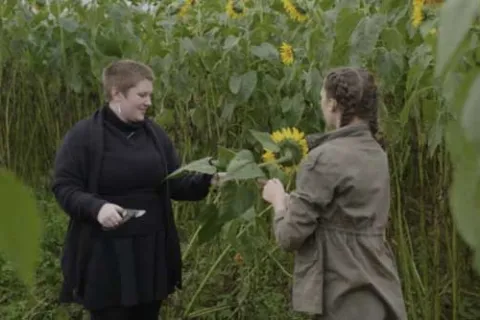 Photo of two women picking sunflowers in a field while on a date