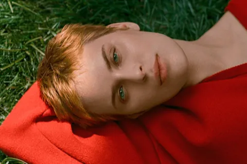 Tallulah Willis laying in the grass wearing a red sweater