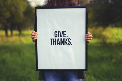 Woman holding a sign that says 'Give Thanks'