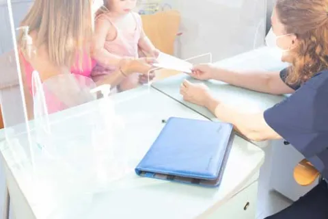 a doctor talking to a mother and child through glass barrier