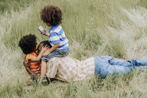 a father laying in a field with his 2 children hugging and sitting on top of him