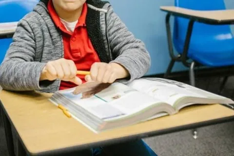 a frustrated child sitting at a desk trying to snap a pencil in half