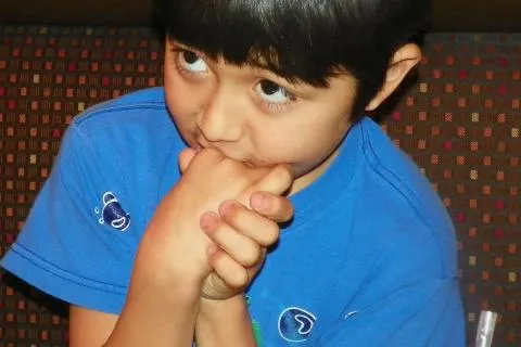 autistic child in a blue shirt putting his hands near his mouth and avoiding eye contact