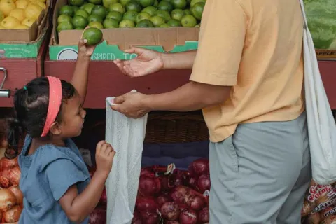 child helping mother put produce in a bag at grocery store