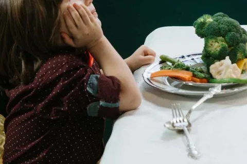 child looking away from a plate of vegetables on the table