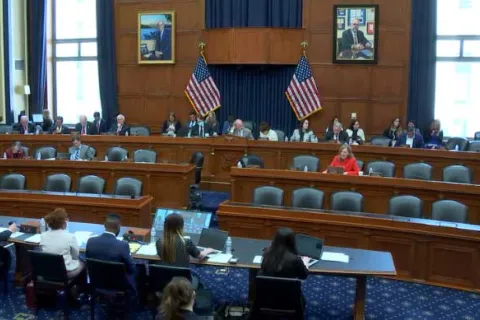 View of committee hearing room, looking at tiered rows of chairs with subcommittee members seated among them