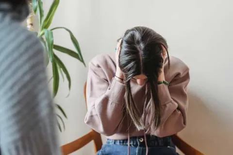 girl in a pink hoodie with her head down and hands covering her ears