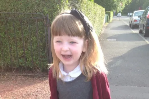 little girl wearing a red cardigan with a bow in her hair