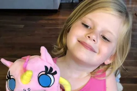 little girl holding a pink stuffed unicorn