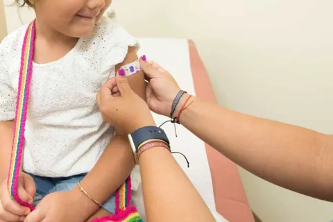 little girl looking down and smiling as a doctor puts a bandage on her arm