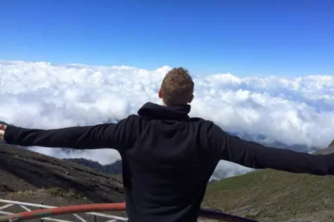 man on a mountain top looking at the clouds