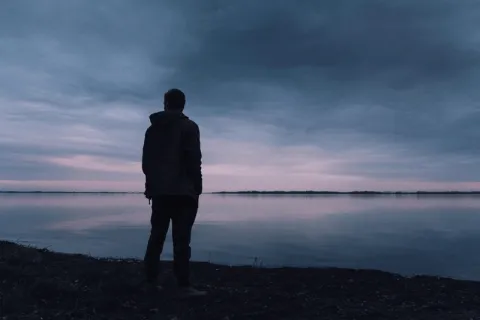 man's silhouette standing in front of a lake at sunset