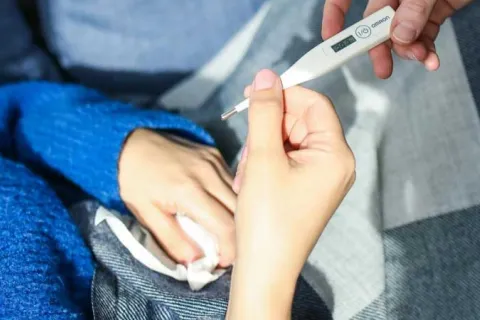 mother handing a thermometer to a child in a blue sweater