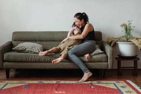 mother laughing and playing with her child on the couch