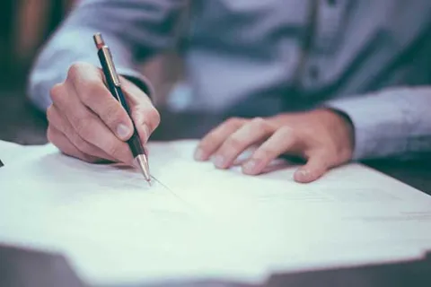 person in a blue button up shirt writing with a pen