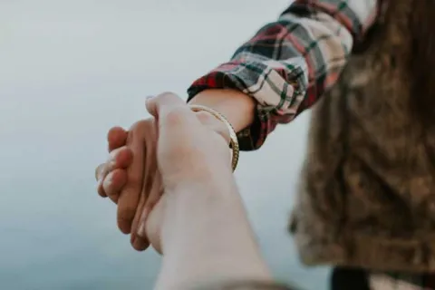 person in a flannel shirt and fur vest holding the hand of someone behind them