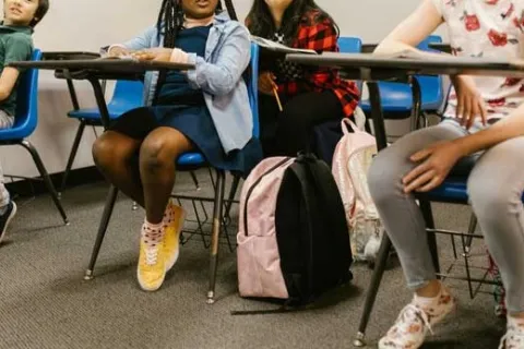 school students sitting in desks with their backpacks at their feet