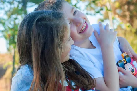 siblings hugging and laughing while playing outside with a Mickey Mouse toy