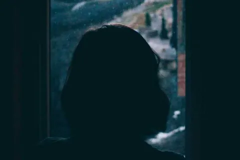 silhouette of a woman looking out the window on a stormy day