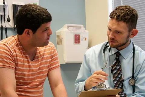 teen in an orange shirt talking to his doctor