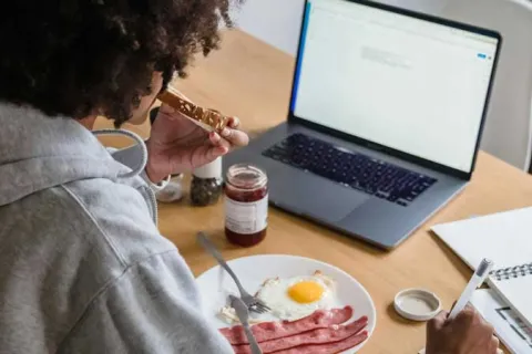 teen sitting at kitchen table eating a working on laptop