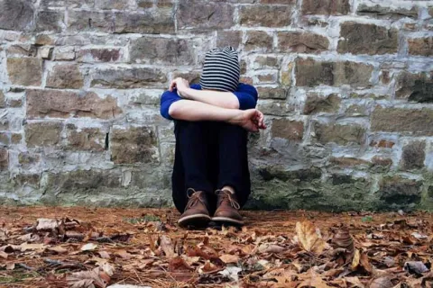 teen sitting on the ground covering their face