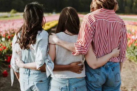 three girls looking at a field of flowers with their arms around each other