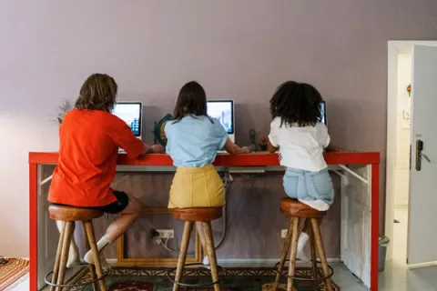 three teens sitting at a table on laptops