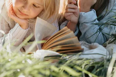 two little girls laying in the grass reading books