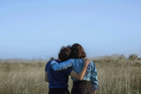 two women with their arms around each other in a field