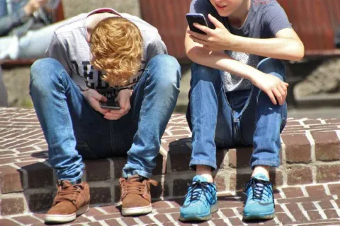 two young boys sitting outside looking at their cell phones