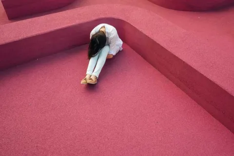 woman in a red room with her head down resting on her knees