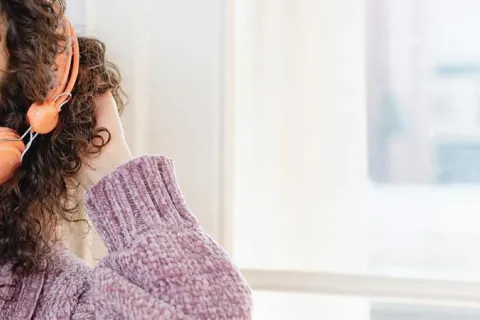 woman touching her curly brown hair and wearing orange headphones