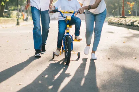 young girl and her parents helping her ride a bike with training wheels 