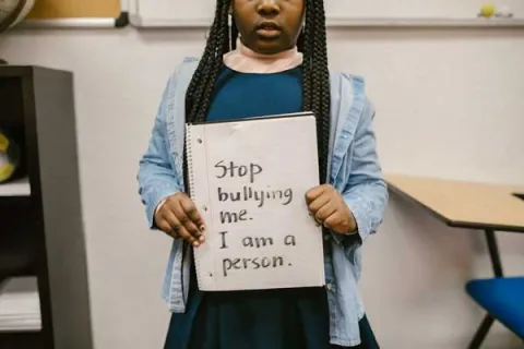 young girl holding a sign that says 'stop bullying me. I am a person'