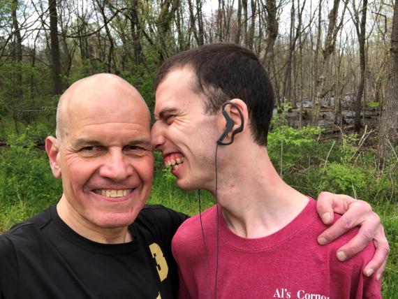 Stuart Spielman looking at camera smiling with arm around his son's shoulder. Zak smiles while leaning his face towards side of Stuart's head.