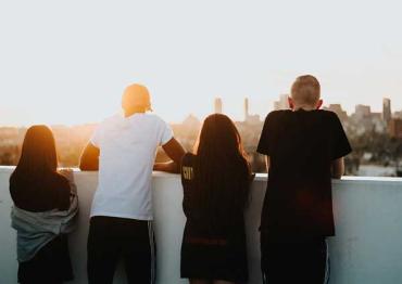 4 teens on a rooftop overlooking a city at sunset