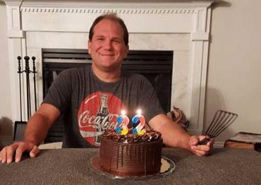 Josh smiling in front of a birthday cake on his 32nd birthday