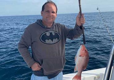 Josh wearing a Batman hoodie on a fishing boat holding up his catch