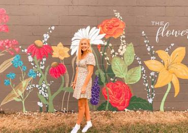 Mallory standing in front of a painted flower mural